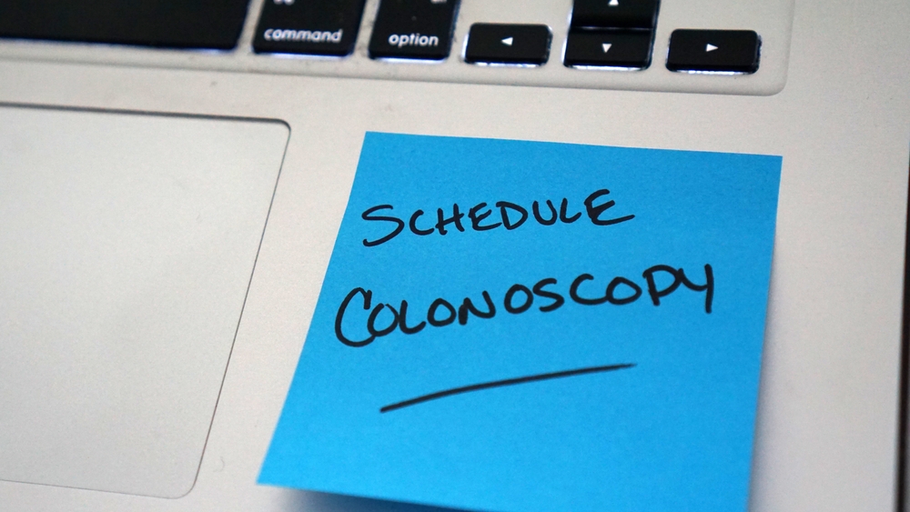 Sticky note reminder on laptop to schedule a colonoscopy                              